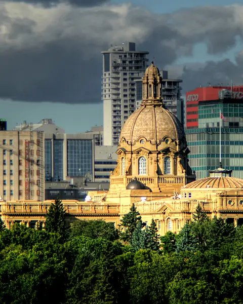 The domed Alberta Legislature Building lit by evening sun in front of downtown Edmonton office towers
