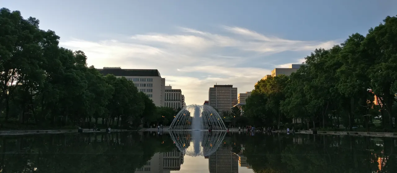 The Alberta Legislature reflecting pool and fountain in Edmonton at dusk, framed by trees and downtown towers