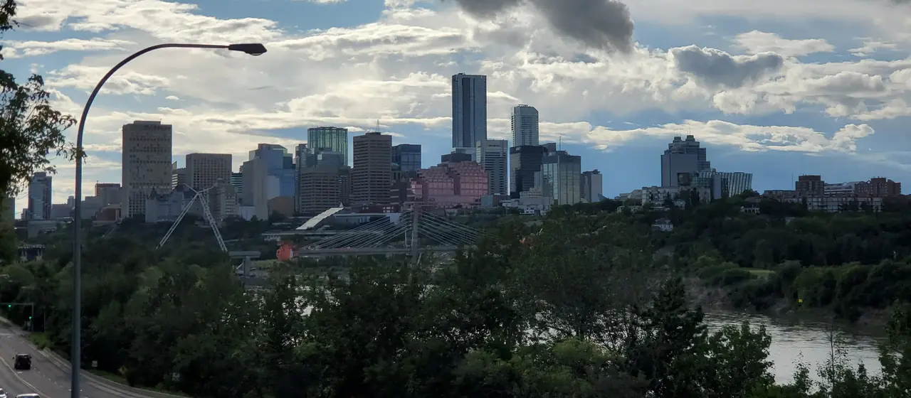 Downtown Edmonton towers rising above the green river valley under dramatic summer clouds