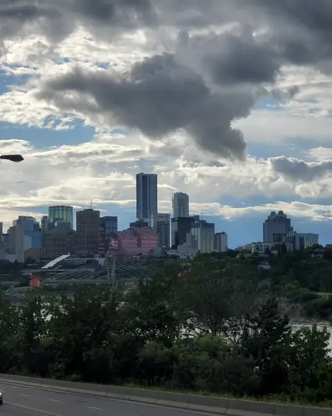 Downtown Edmonton towers rising above the green river valley under dramatic summer clouds