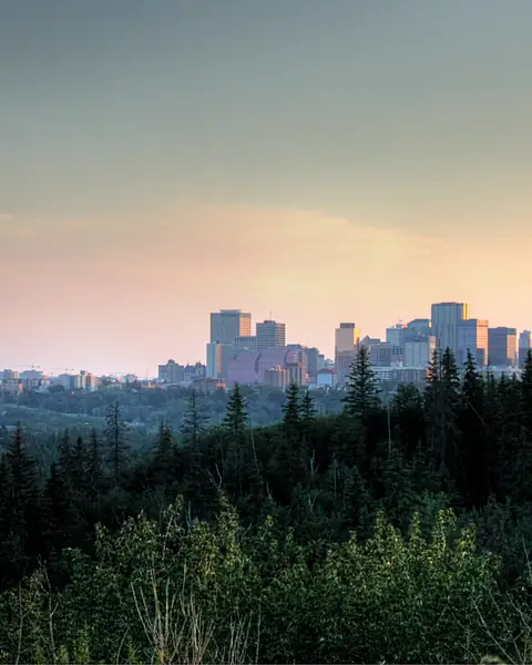 Forested North Saskatchewan River valley at dusk with the distant downtown Edmonton skyline, seen from Highlands