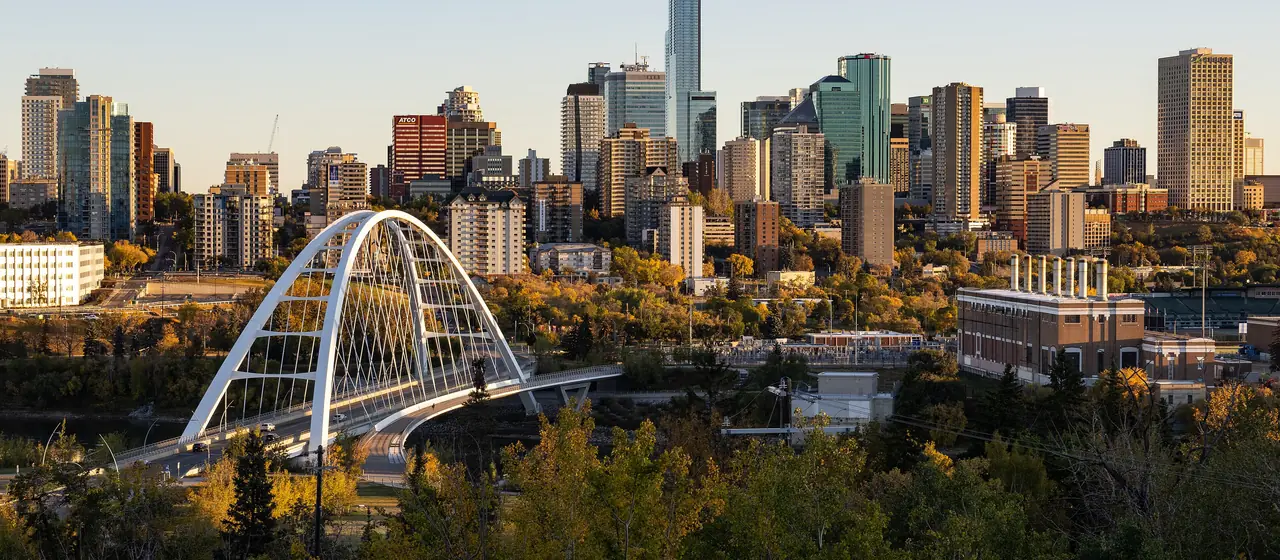 The white arch of the Walterdale Bridge crossing the river valley into the downtown Edmonton skyline in early autumn